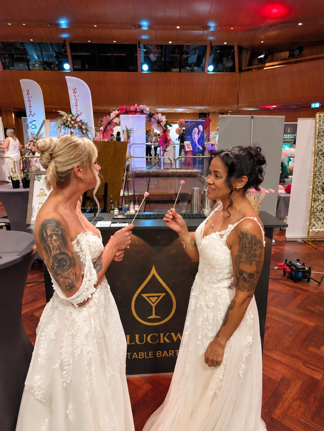 Zwei Bräute in Brautkleidern vor der mobilen Cocktailbar von Schluckwerk auf einer Hochzeitsmesse